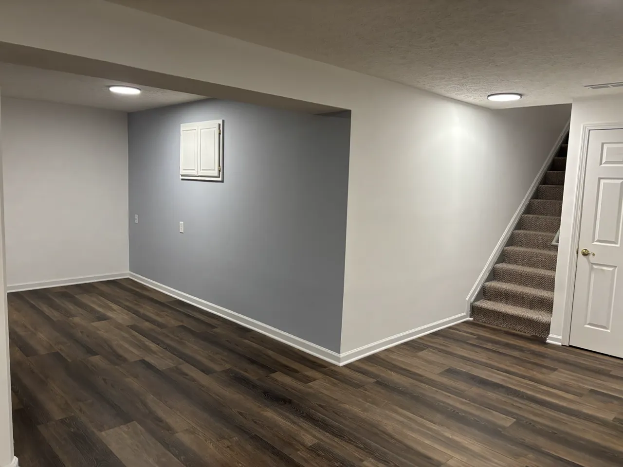Finished basement with wood-look plank flooring, blue accent wall, and staircase
